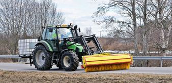 Harjalakaisukalustolla varustettu traktori puhdistaa autotietä.
