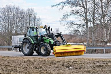 Lakaisukalustolla varustettu traktori puhdistamassa autotietä.
